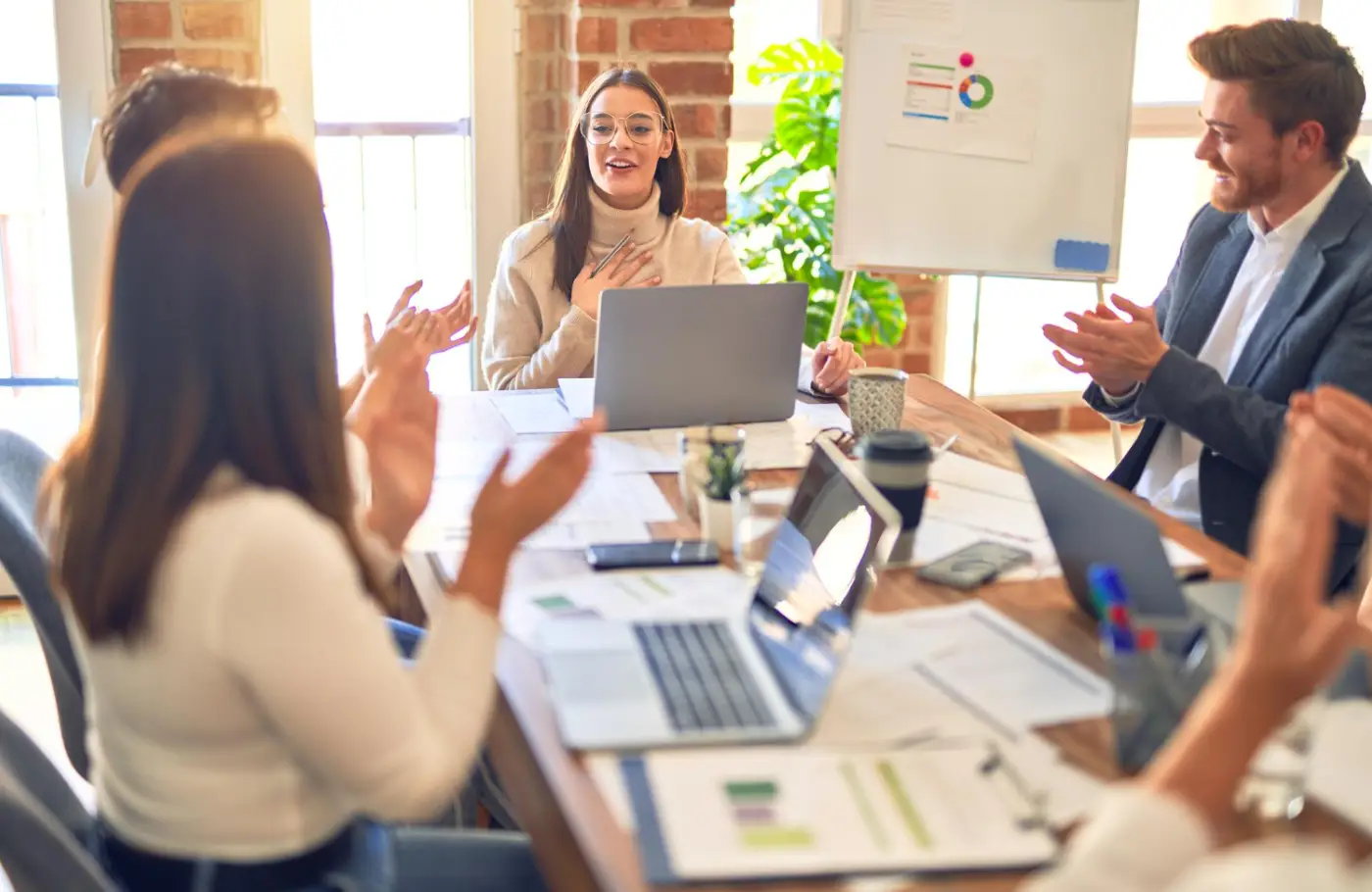 A group of professionals engaged in a meeting, clapping and discussing strategies, with laptops and documents on the table A group of professionals engaged in a meeting, clapping and discussing strategies, with laptops and documents on the table